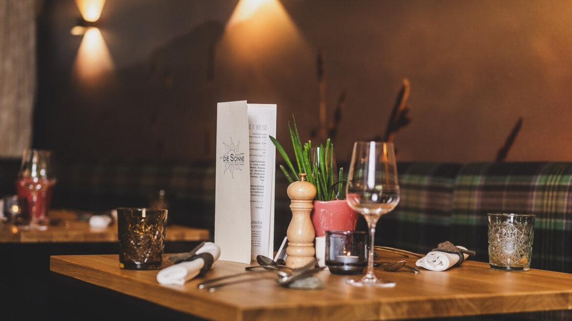 Ein ordentlich gedeckter Tisch im Restaurant des Hotels Sonne mit Speisekarten, Gläsern, Besteck, einer Pfeffermühle und einer kleinen Pflanze. (vergrößerte Ansicht)