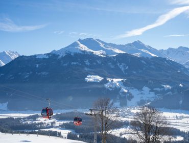 Rote Seilbahnen fahren über eine verschneite Berglandschaft unter einem strahlend blauen Himmel.