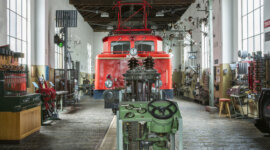 Eine rote Dampflok aus vergangenen Zeiten in einem Museum in Schwarzach im Pongau, umgeben von alten Maschinen und Werkzeugen, die dort ausgestellt sind.