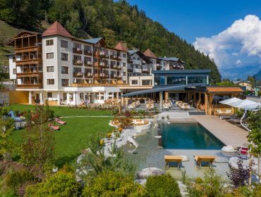 Das Sportresort Alpenblick ist ein großes Hotel mit Balkonen mit Blick auf einen Naturpool, Gärten und Berge.