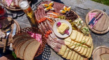 Eine Holzplatte mit kulinarischen Köstlichkeiten - Fleisch, Käse und Bier - fängt den Geist des Almsommers ein.