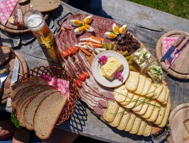 Brettljause Praeau Hochalm (c) Gasteinertal Tourismus GmbH, Christoph Oberschneider Eine Holzplatte mit kulinarischen Köstlichkeiten - Fleisch, Käse und Bier - fängt den Geist des Almsommers ein.