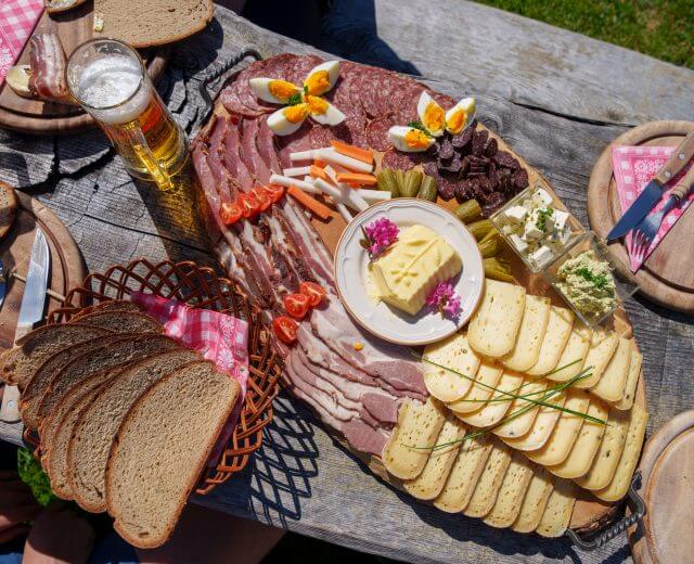 Brettljause Praeau Hochalm (c) Gasteinertal Tourismus GmbH, Christoph Oberschneider Eine Holzplatte mit kulinarischen Köstlichkeiten - Fleisch, Käse und Bier - fängt den Geist des Almsommers ein.