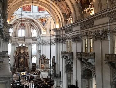 Das Innere einer großen Kathedrale mit verschnörkelten Bögen, hohen Decken und darunter versammelten Menschen.