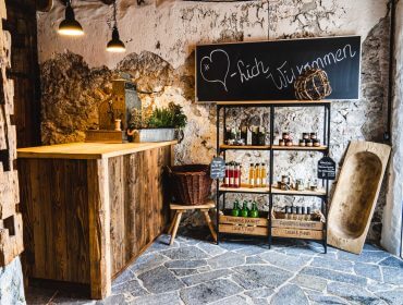 Rustikaler Marktstand mit Holztheke, Regalen mit Gläsern und Flaschen und "Herzlich Willkommen" auf Kreidetafel.