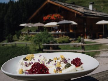 Eine Platte mit Gourmet-Käse mit Kräutern und Gelee, im Freien mit einer rustikalen Hütte im Hintergrund.