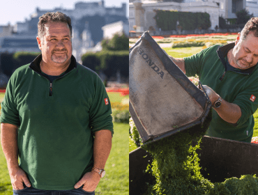 Ein Mann in einem grünen Pullover steht im Freien und wirft Grasschnitt in einen Container in einem sonnigen Park.