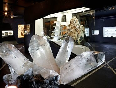 Große Quarzkristalle in einer modernen, schwach beleuchteten Ausstellung des Mineralien- und Geologiemuseums Locandy-Guide.
