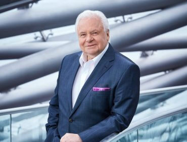 Hangar-7; Falstaff; Eckart Witzigmann; Ein älterer Mann im Anzug steht an einem Glasgeländer mit einem modernen architektonischen Hintergrund.