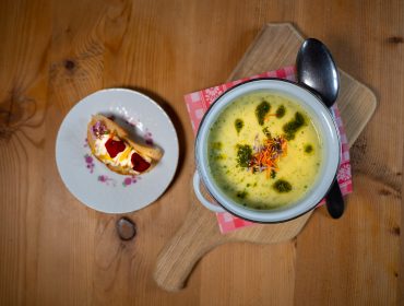 Schale mit cremiger Suppe mit grüner Garnierung, serviert mit einer Brotscheibe auf einem Teller, auf einem Holztisch.