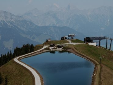 Ein Bergstausee mit Skiliften, umgeben von Bergen und einem Waldgebiet.