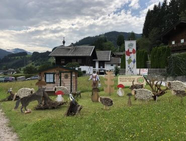 Dekorative Tier- und Pilzausschnitte auf Gras in der Nähe eines kleinen Hauses, Berge und Bäume im Hintergrund.