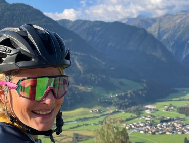 Your Choice – Bike-Genuss in der Wildkogel-Arena, Bike Stories im SalzburgerLand Lächelnder Radfahrer mit Helm und Sonnenbrille vor einem malerischen Bergtal im Hintergrund.