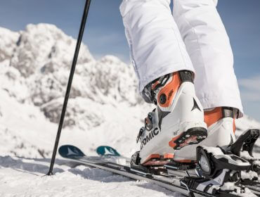 Nahaufnahme eines Skifahrers, der seine Schuhe in die Skier schnallt, auf einem verschneiten Berg mit strahlend weißem Schnee und blauem Himmel.