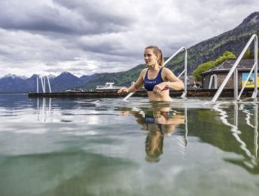 Eine Frau im Badeanzug klettert über eine Metallleiter aus einem See, umgeben von Bergen, Wolken und Nachhaltigkeit.