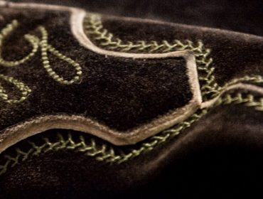 Nahaufnahme eines dunklen Wildlederstoffs mit grünen Ziernähten und Stickereien.