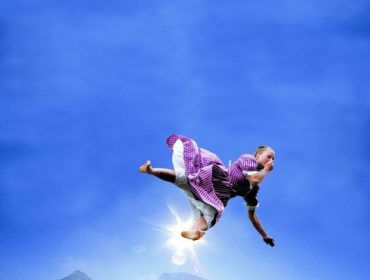 Ein Mädchen in einem Kleid scheint in der Luft über einem See und Bergen unter einem strahlend blauen Himmel zu schweben.