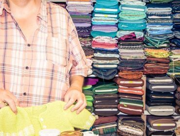 Eine Person, die vor einem Regal mit bunten gefalteten Textilien Stoff faltet.