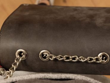 Eine Nahaufnahme einer schwarzen Tasche mit silbernem Kettenriemen und rosa Quaste, von oben gesehen.