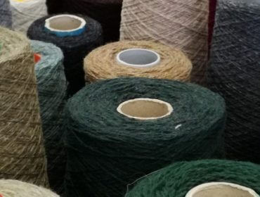 Mehrere Garnspulen in verschiedenen Farben sind, von oben betrachtet, dicht aneinander gereiht.