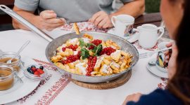 Restaurant Fuschertörl Menschen teilen sich eine Pfanne mit Kaiserschmarrn und Beeren an einem für das Frühstück gedeckten Tisch im Freien.