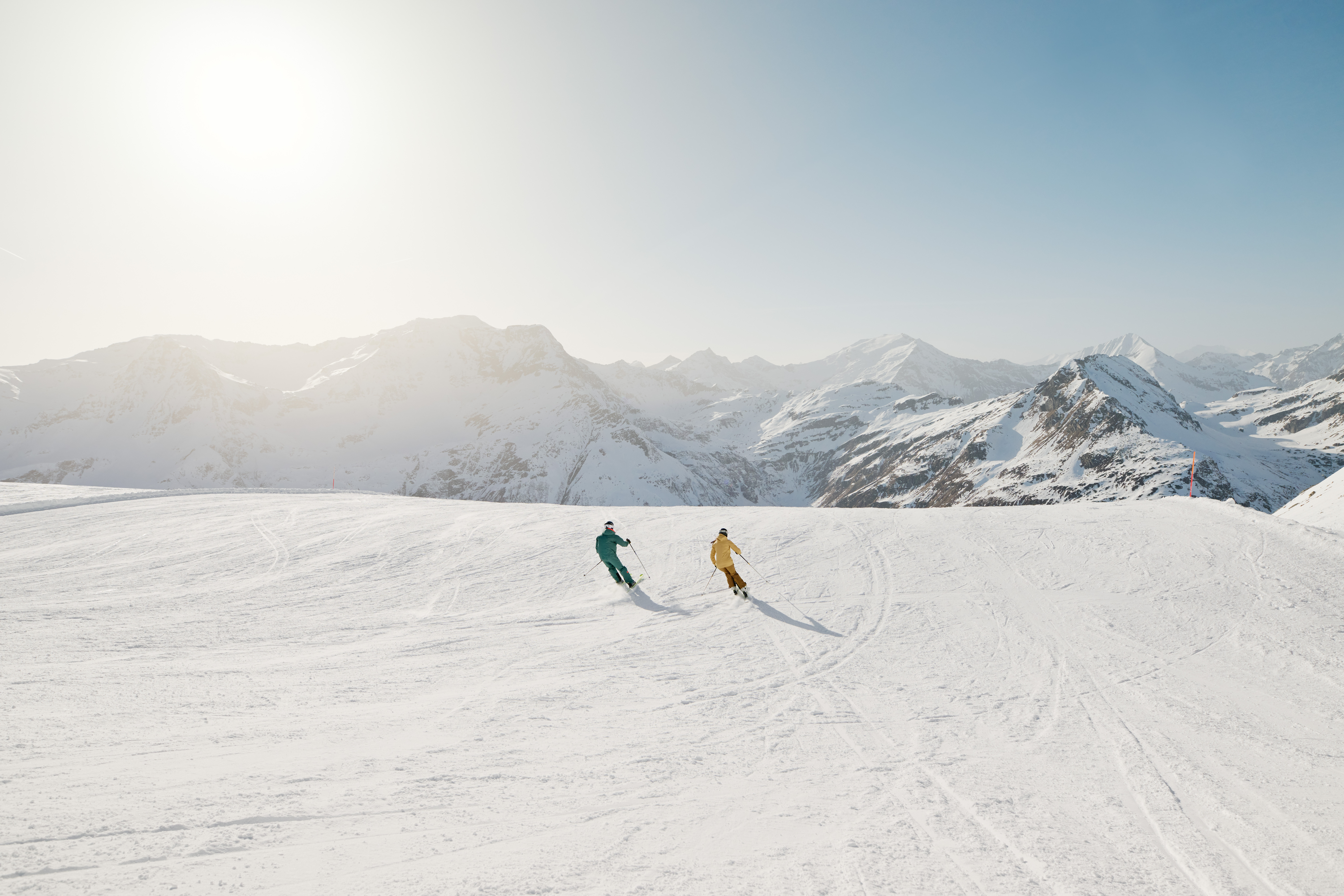 Zwei Skifahrer auf einem verschneiten Hang mit Bergen im Hintergrund.
