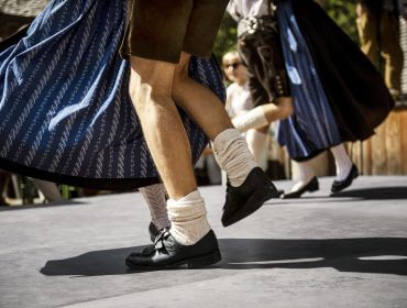 Menschen in österreichischer Tracht führen im Freien einen Volkstanz auf, bei dem ihre Beine und Füße im Mittelpunkt stehen.