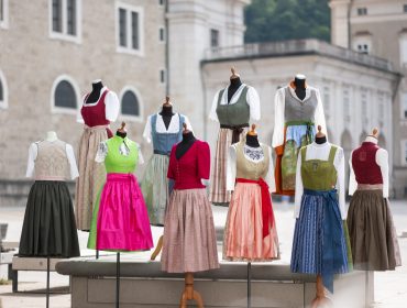 SLT_Bauernherbstdirndl-46 Schaufensterpuppen zeigen traditionelle bunte Kleider auf einem europäischen Stadtplatz im Freien.