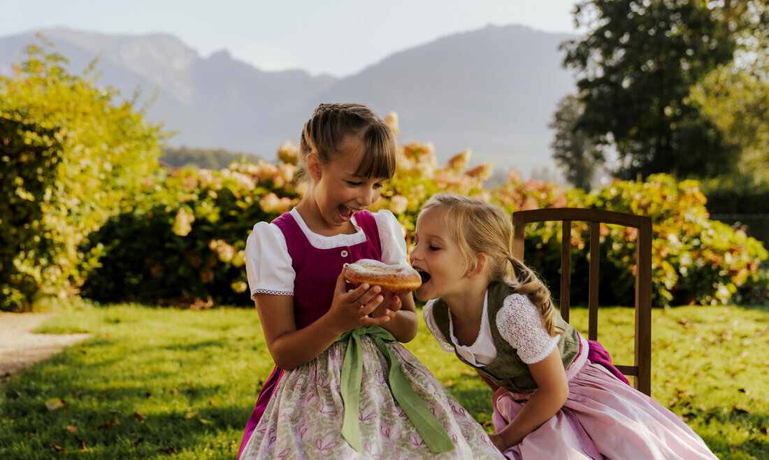 Bauernherbst im SalzburgerLand, zwei Kinder im Dirndkleid essen einen Bauernkrapfen