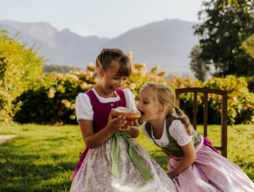 Bauernherbst im SalzburgerLand, zwei Kinder im Dirndkleid essen einen Bauernkrapfen