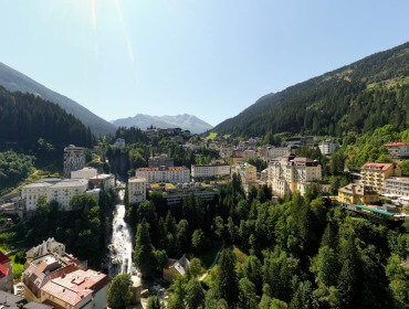 Eine malerische Stadt, eingebettet in grüne Berge, mit einem Wasserfall in der Mitte, der unter einem klaren Himmel fließt.