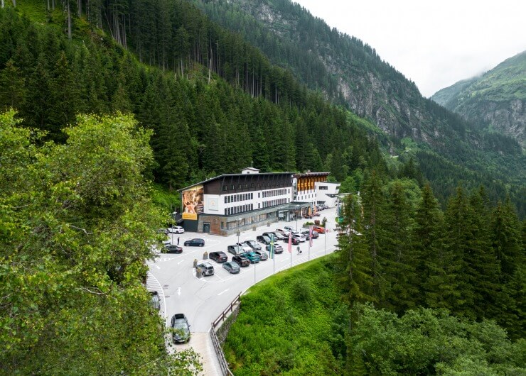 Ein Hotel mit geparkten Autos davor, umgeben von dichtem grünen Wald und Bergen.