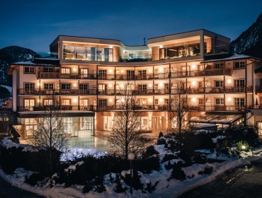 Ein großes, gut beleuchtetes Hotel mit Balkonen, umgeben von Schnee, bei Nacht in einer Bergregion.