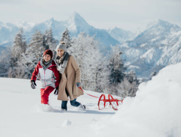 Mutter und Tochter ziehen einen roten Schlitten durch den Schnee