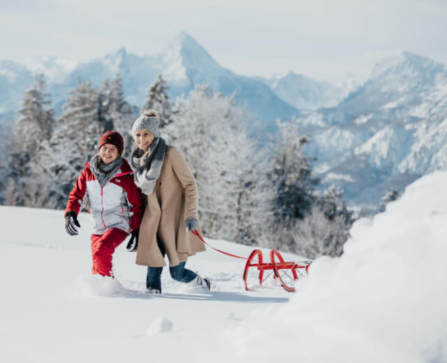 Familie im Schnee Mutter und Tochter ziehen einen roten Schlitten durch den Schnee