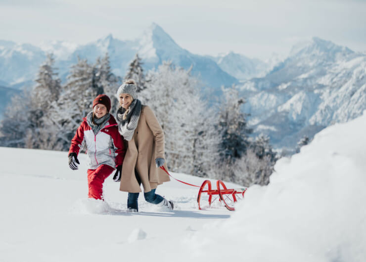Mutter und Tochter ziehen einen roten Schlitten durch den Schnee