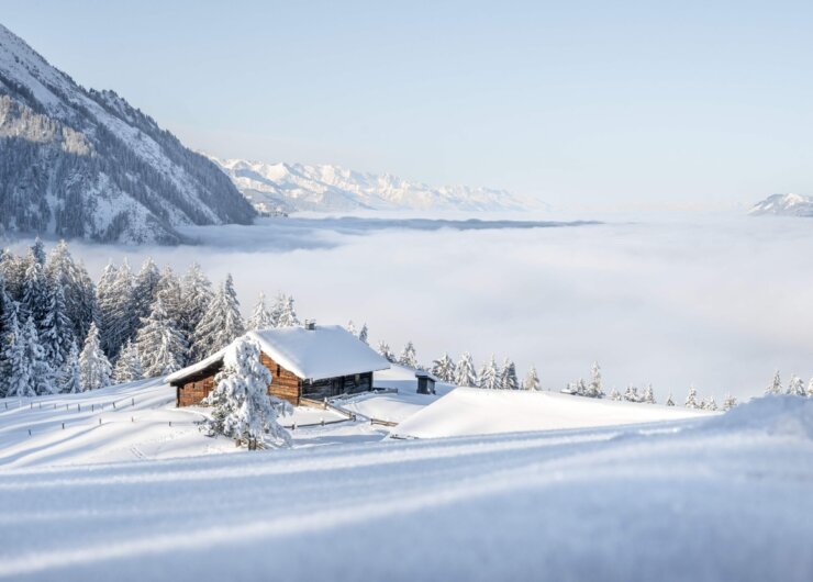 Holzhütte in einer verschneiten Berglandschaft über einem Meer aus Wolken.