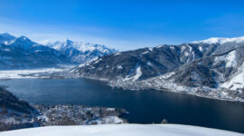 Hauptmotiv Mitterbergblick © Zell am See-Kaprun Tourismus.d237f04a_original Ein schneebedecktes Dorf und ein See, umgeben von Bergen unter einem strahlend blauen Himmel.