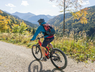 Radfahren im Salzkammergut Ein Radfahrer fährt mit seinem Mountainbike auf einem Schotterweg am Wolfgangsee, mit malerischen Bergen und Bäumen im Hintergrund.