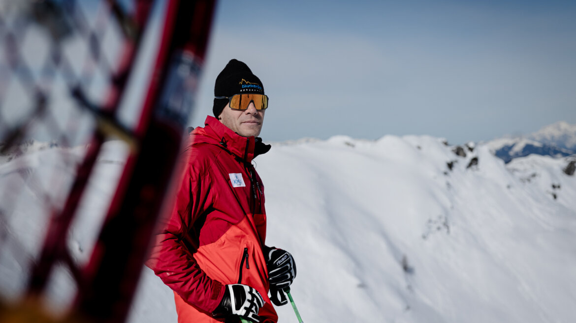 Michael Walchhofer mit schwarzer Mütze und Skibrille im Portrait. Im Hintergrund sieht man verschneite Berge.