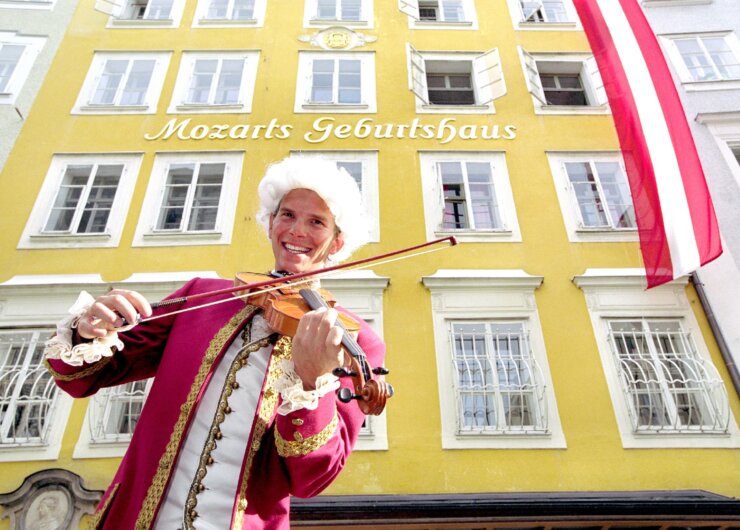 Ein Mann in einem historischen Kostüm spielt Geige auf dem Mozart-Radweg in der Nähe von Mozarts Geburtshaus in Salzburg, Österreich.