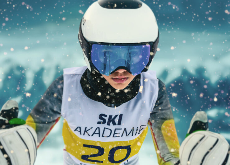 Ein Skifahrer in Rennausrüstung und mit Skibrille fährt durch fallenden Schnee und trägt ein Trikot der Ski Akademie.