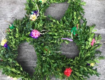 Grüner Blätterkranz mit bunten kleinen Blumen liegt auf einer grauen Holzfläche.