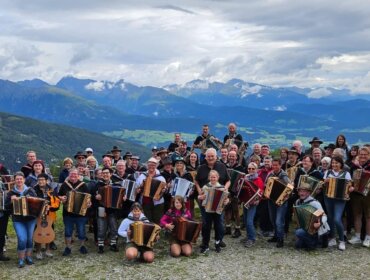 Eine große Gruppe von Menschen mit Akkordeons posiert auf einem Berg mit malerischer Aussicht und bewölktem Himmel im Hintergrund.