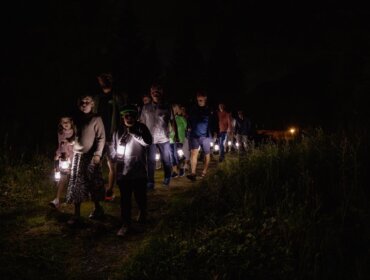 Eine Gruppe von Menschen geht nachts auf einem dunklen Weg und trägt Laternen, die ihren Weg beleuchten.