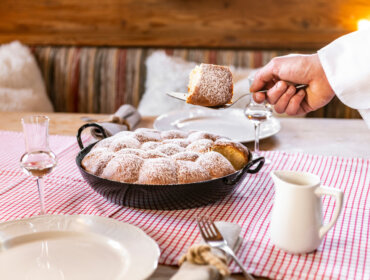 Eine Hand serviert ein Stück Kuchen mit Puderzucker und bringt kulinarischen Charme auf ein kariertes Tischtuch.