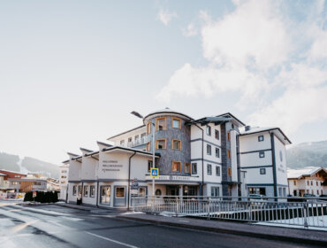 Modernes alpines Hotelgebäude mit weißem und grauem Äußeren, das an einem klaren Wintertag neben einer Straße liegt.