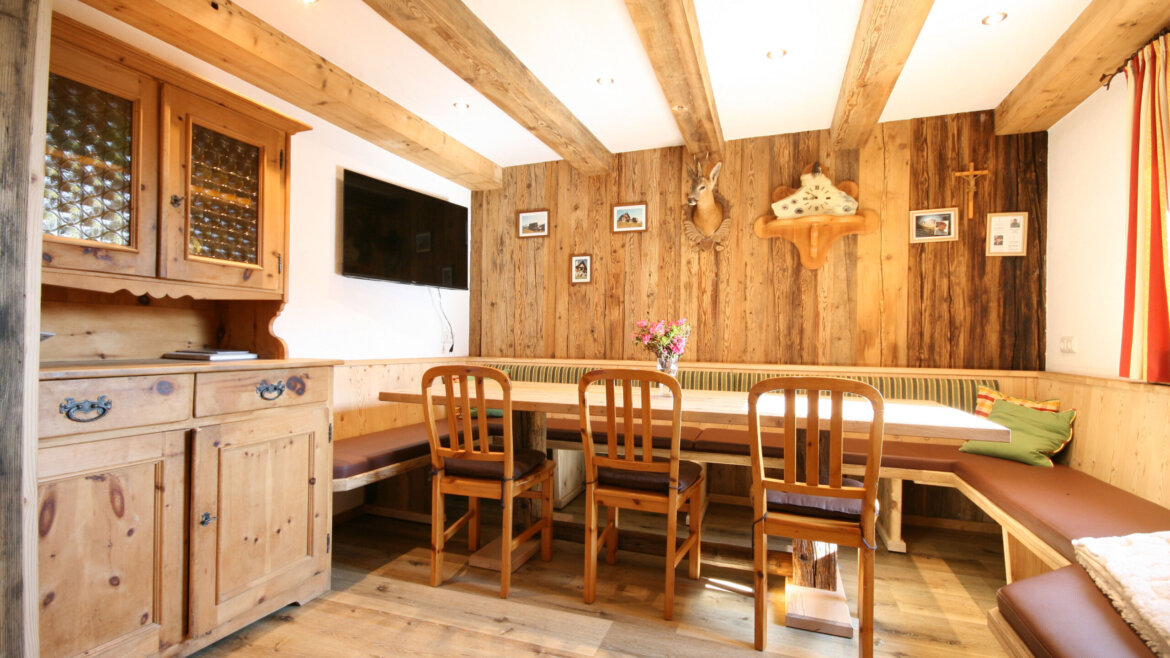 Gemütliches Esszimmer aus Holz mit einem langen Tisch, vier Stühlen, einer Bank und rustikalem Dekor an den Wänden. (vergrößerte Ansicht)