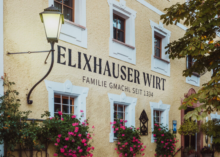 Gelbes Gebäude mit weiß umrandeten Fenstern, Blumen und einem Schild mit der Aufschrift Elixhauser Wirt Familie Gmachl seit 1334.