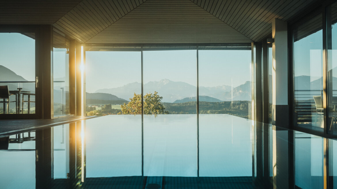 Innenpool mit Blick auf die Berge durch große Glasfenster bei Sonnenaufgang oder Sonnenuntergang. (vergrößerte Ansicht)